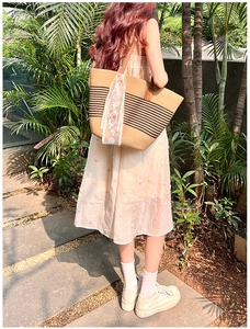 Straw tote bag detail with floral lace ribbon and brown leather handle in a garden setting
