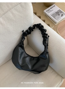 Detail of a black crescent hobo bag featuring a pleated scrunchie strap on a cream sofa