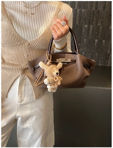 Close-up of a coffee brown leather handbag with a plush bear charm on a stone background