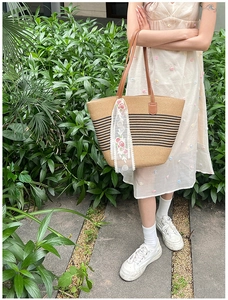 Detail of woven straw tote bag with black stripes, brown leather handles and lace scarf