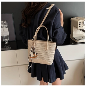 Dettaglio della borsa tote beige intrecciata con ciondolo a cavallo in un interno neutro