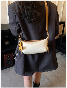 Détail d'un sac bandoulière beige crème texturé litchi avec un charm cheval jaune