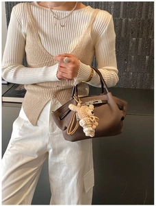 Detail of a brown leather tote bag with litchi grain and a cute knitted bear charm