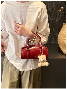 Gros plan d'un sac Boston en cuir verni rouge foncé avec logo doré et charm d'ours en peluche