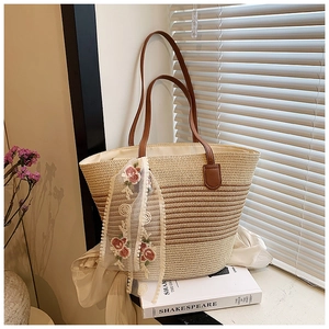 Detail of woven straw tote bag with gradient tones and embroidered lace scarf accessory