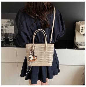 Dettaglio della borsa tote intrecciata beige con manico in pelle e ciondolo