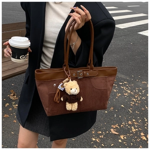 Detail of brown suede tote bag with leather straps and cute bear charm in autumn setting