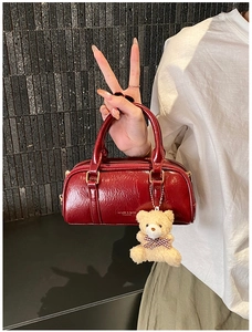 Détail du sac Boston en cuir verni bordeaux avec zip doré et breloque petit ours