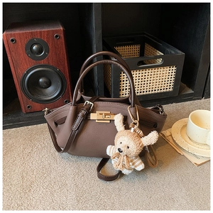 Detail of dark brown leather tote bag with gold clasp and cute teddy bear charm accessory