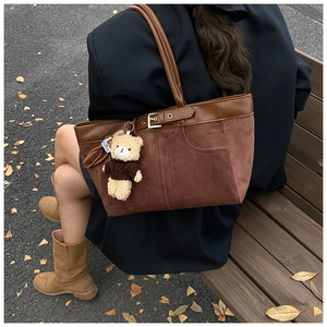 Detail of dark brown suede tote bag with pocket design and cute bear charm outdoors