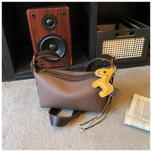 Détail du sac à bandoulière en cuir marron avec breloque cheval jaune sur tapis gris
