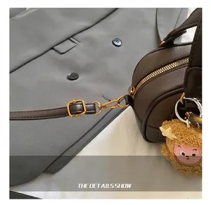 Detail of gold metal hook and leather strap on a dark brown square crossbody bag