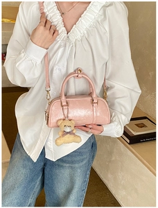 Detail of pink Boston bag with leather texture and plush bear charm worn by a model
