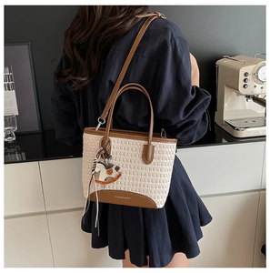 Dettaglio della borsa tote intrecciata beige con finiture in pelle marrone e ciondolo