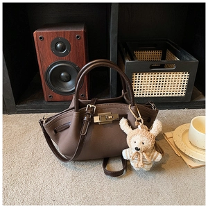 Detail of dark brown leather tote with fine texture, golden lock, and a woven charm
