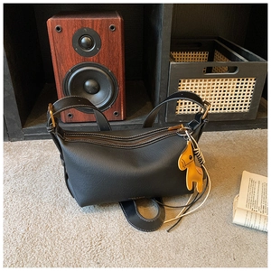 Détail d'un sac demi-lune noir avec coutures blanches contrastées et breloque cheval jaune