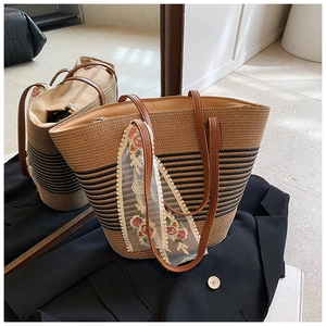 Detail of straw tote bag featuring black stripes and floral lace ribbon accessory