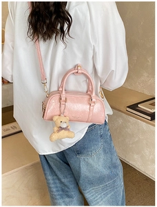 Rear view of a pink glossy Boston bag with a teddy bear charm on a model's shoulder