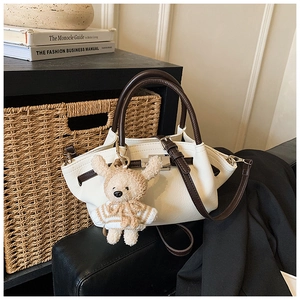 Detail of white lychee pattern crossbody bag with brown handles and a plush bear charm