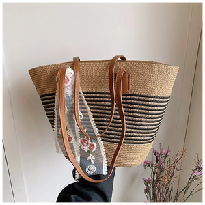 Close-up of woven straw tote bag with black stripes and floral lace scarf detail