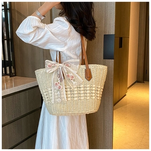 Detail of straw tote bag featuring white lace bow, floral embroidery and leather handles
