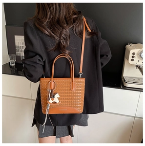 Dettaglio borsa tote intrecciata marrone con tracolla e ciondolo a cavallo sul modello