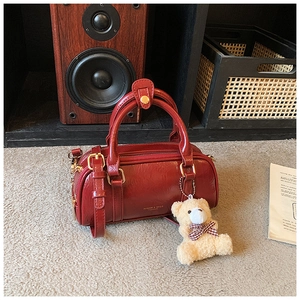 Détail du sac cylindre rouge brillant avec breloque d'ours en peluche et boucles dorées