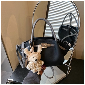Close-up of black lychee leather tote bag with silver clasp and cute plush bear charm