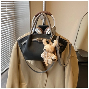 Detail of black leather handbag with a gray handle, knit charm, and metal twist lock