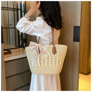 Detail of woven straw tote bag featuring white lace bow and floral embroidery handles