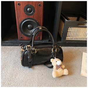 Détail d'un mini sac à main en cuir verni noir plissé avec garnitures dorées et ours en peluche