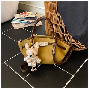 Close-up of mustard yellow pebble leather bag with silver turn-lock and cute bear charm