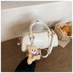 Détail du sac Boston en cuir verni blanc avec texture craquelée et breloque ours en peluche
