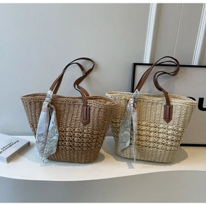 Detail of woven straw tote bag with brown leather handles and decorative silk scarf accessory