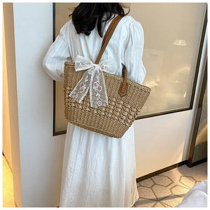 Detail of hand-woven straw tote with white lace bow and floral embroidery decoration