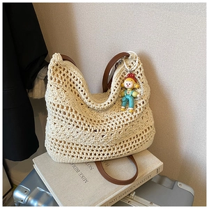 Dettaglio della borsa intrecciata con tracolla in pelle marrone e ciondolo