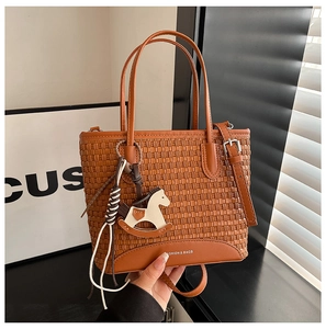 Dettaglio della borsa tote intrecciata marrone con finiture in pelle e ciondolo