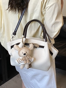 Cream textured leather tote bag with brown handles and a crochet bear charm on a model