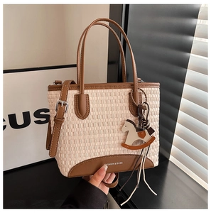 Dettaglio della borsa tote intrecciata con finiture in pelle marrone e ciondolo a cavallo