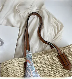 Detail of woven straw tote bag featuring leather handles and a geometric pattern silk scarf