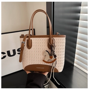 Dettaglio borsa tote intrecciata beige con finiture in pelle marrone e ciondolo