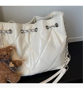 Detail of quilted beige leather bucket bag with metal chain drawstring and teddy bear charm