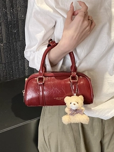 Sac Boston en cuir verni rouge foncé avec pendentif ours en peluche et détails dorés