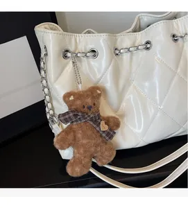 Detailed macro shot of white quilted tote bag featuring a silver chain and plush bear charm