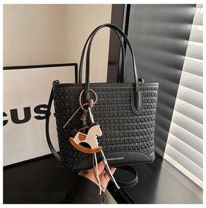 Dettaglio della borsa tote nera intrecciata con finiture in pelle e ciondolo in legno