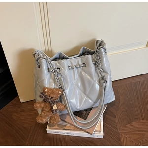 Close-up of quilted chain bucket bag with plush bear charm on wooden floor