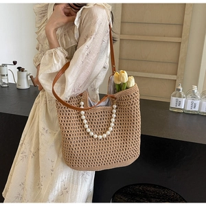 Detail of straw woven tote bag featuring pearl chain strap and brown leather handles