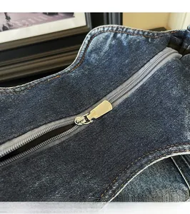 Detail of silver metal zipper with orange stitching on blue denim shoulder bag