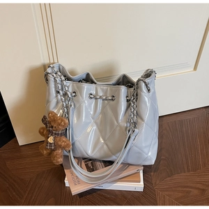 Detail of light gray quilted chain bucket bag with a cute plush bear charm accessory