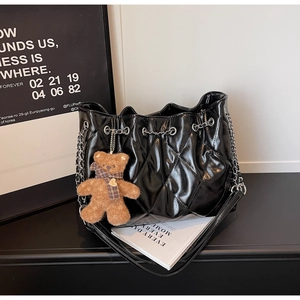 Detail of black quilted bucket bag with silver chain strap and plush bear charm